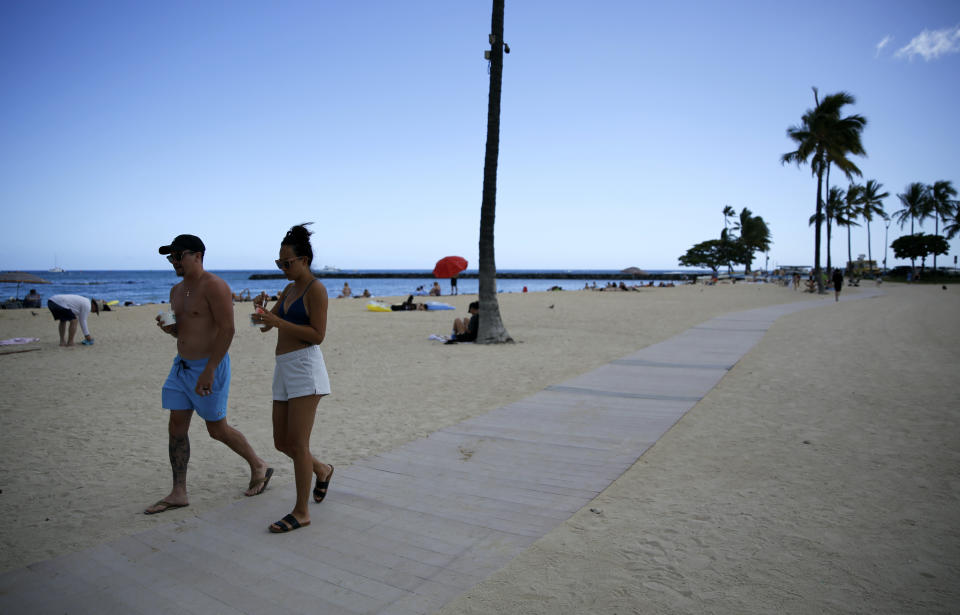 Honeymooners Samantha Hanberg, right, and Brian Swan eat shave ice while walking along Waikiki Beach in Honolulu, Monday, May 23, 2022. A COVID surge is under way that is starting to cause disruptions as schools wrap up for the year and Americans prepare for summer vacations. Case counts are as high as they've been since mid-February and those figures are likely a major undercount because of unreported home tests and asymptomatic infections. But the beaches beckoned and visitors have flocked to Hawaii, especially in recent months. (AP Photo/Caleb Jones)