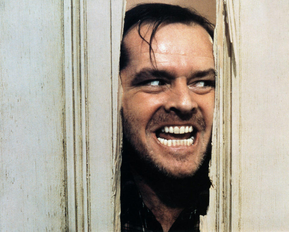 Jack Nicholson peers through a broken door with a manic expression, reenacting a famous scene from "The Shining."