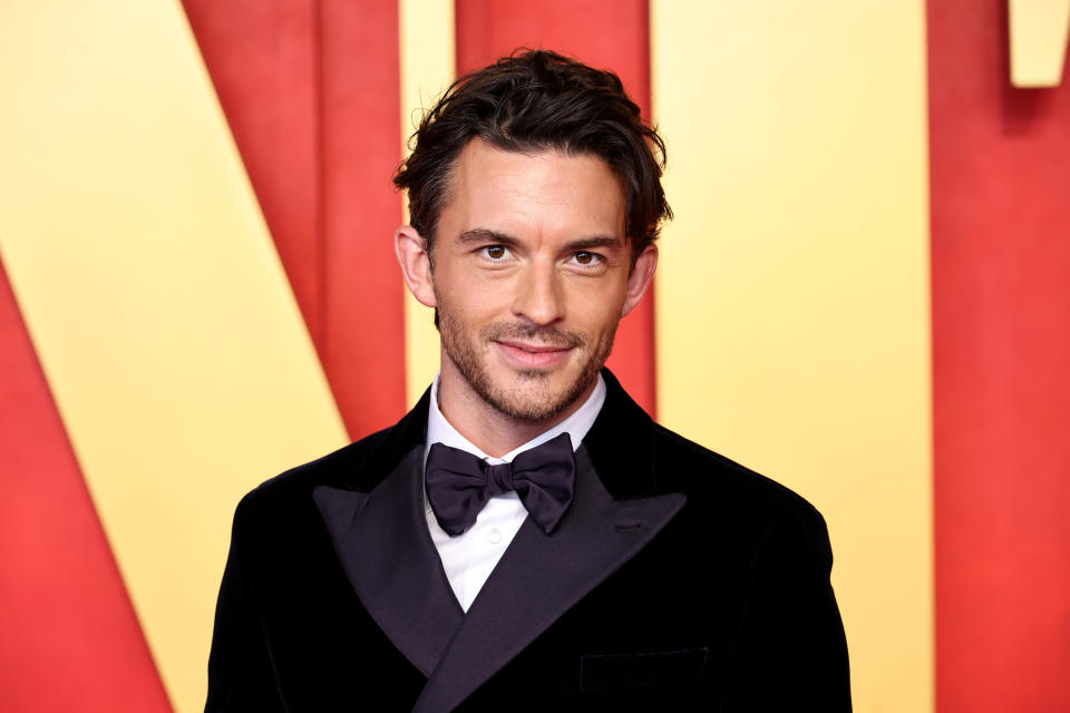 Jonathan Bailey poses in a black tuxedo with bow tie on a red carpet