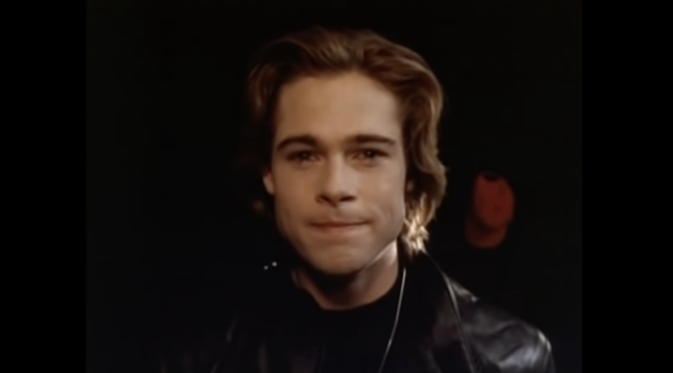 A young Brad Pitt wears all black and is looking directly into the camera with a small smile