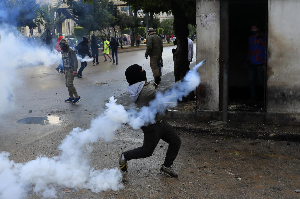 A protester throws back a tear gas canister towards riot policemen during a protest against deteriorating living conditions and strict coronavirus lockdown measures, in Tripoli, north Lebanon, Thursday, Jan. 28, 2021. Violent confrontations between protesters and security forces over the last three days in northern Lebanon left a 30-year-old man dead and more than 220 people injured, the state news agency said Thursday. (AP Photo/Hussein Malla)