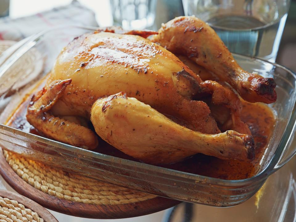 A cooked whole turkey sits in a dish next to a head of garlic on a Thanksgiving table