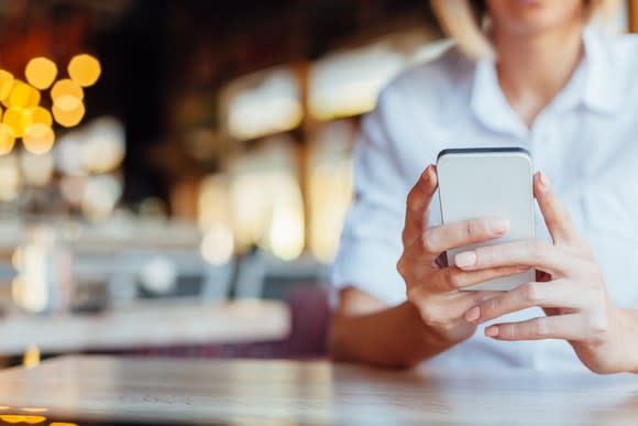 A woman sitting at a table holding and looking at a mobile phone.