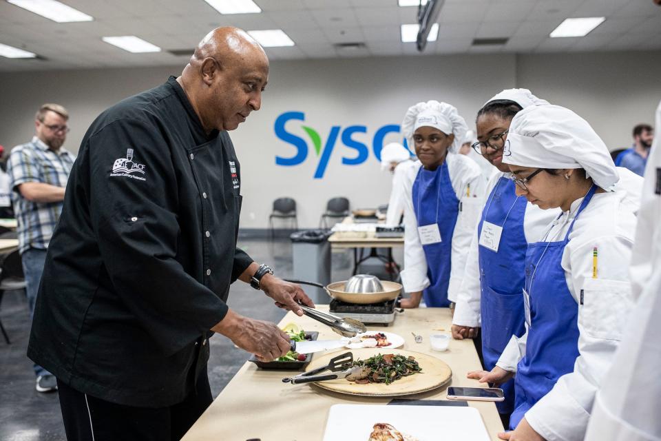 Jimmy Lee Hill, executive chef instructor, left, demonstrates plating dishes made by a group of students during Michigan ProStart program's Mise en Place Bootcamp at Sysco Detroit in Canton on Friday, Jan. 13, 2023.