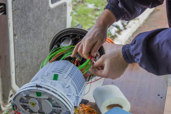 A technician attaching fiber-optic cable bundles to a piece of wireless networking equipment.