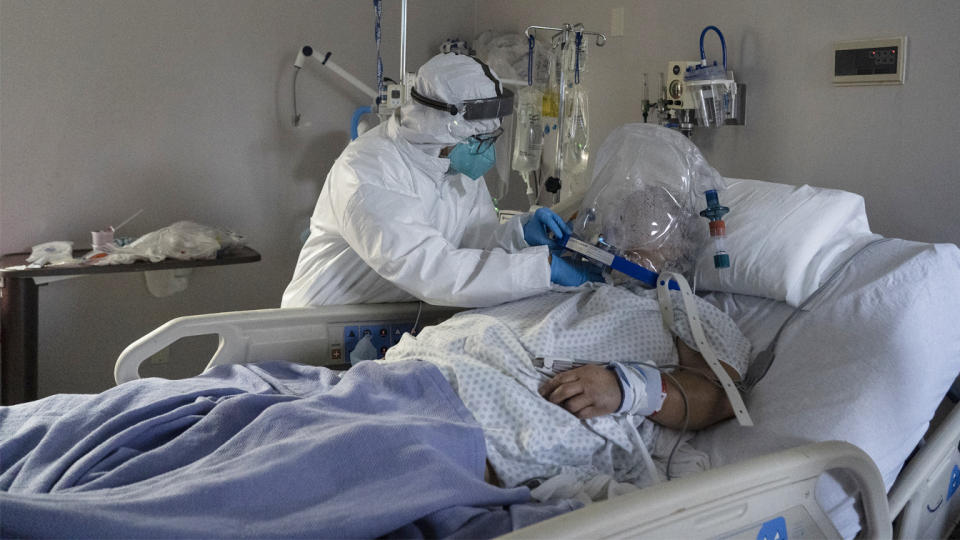 A member of the medical staff treats a patient who is wearing a helmet-based ventilator