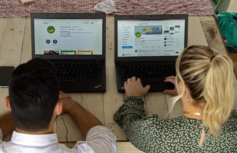 Leonardo de Carvalho Leal, left, and Mayara Stelle, who administer the Twitter account Sleeping Giants Brazil, use their computers in Sao Paulo, Brazil, Friday, Dec. 11, 2020. Sleeping Giants is a platform for activism whose stated mission is to attack the financing of hate speech and dissemination of fake news. (AP Photo/Andre Penner)