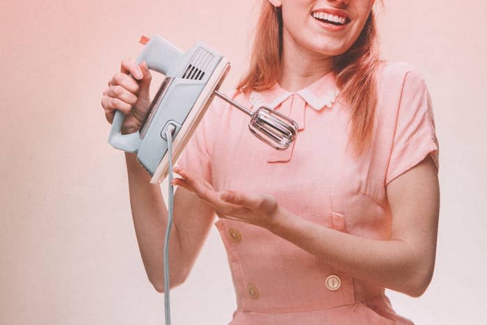 woman dressed like a vintage homemaker holding a hand mixer