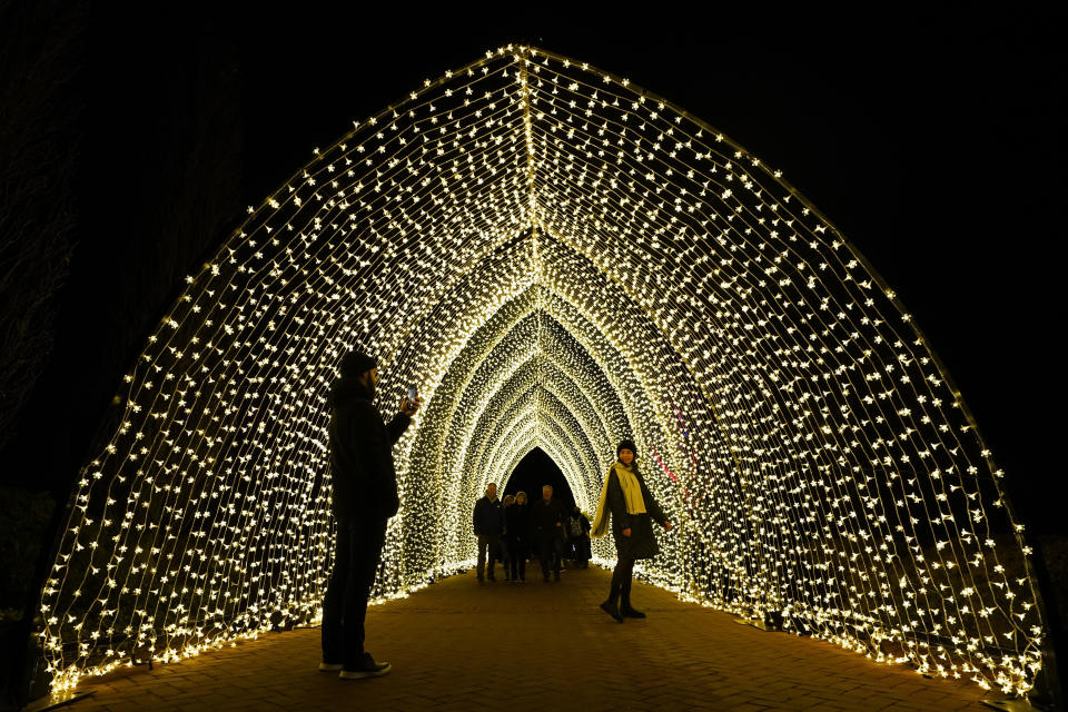 Roma Di, left, takes a picture of Irene Kin, both recently arriving from Ukraine, as they finish the 1.3-mile Lightscape experience of light and music inside the 110-foot, 100,000 lights of "Winter Cathedral," created by Mandylights, at the Chicago Botanic Garden in Glencoe, Ill., on Thursday, Dec. 14, 2023. (AP Photo/Charles Rex Arbogast)