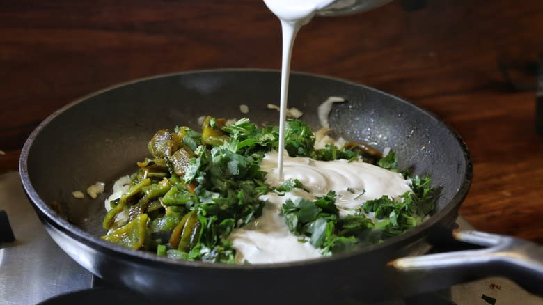 pouring cream into skillet of peppers