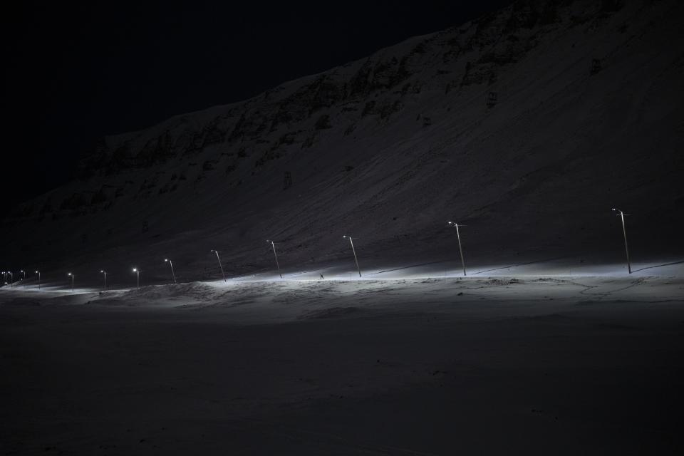 Un esquiador avanza junto a un camino iluminado durante la noche polar en Longyearbyen, Noruega, el viernes 6 de enero de 2023. Tan cerca del Polo Norte, el sol está al menos seis grados bajo el horizonte de mediados de noviembre hasta finales de enero. (AP Foto/Daniel Cole)