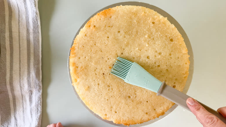 Brushing almond simple syrup onto Chantilly cream cake