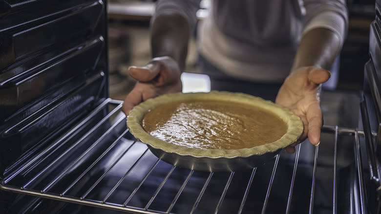 hands placing pumpkin pie in oven