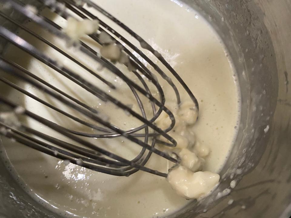 whisk breaking up chunks of blue cheese in a butter sauce in a pot on the stove