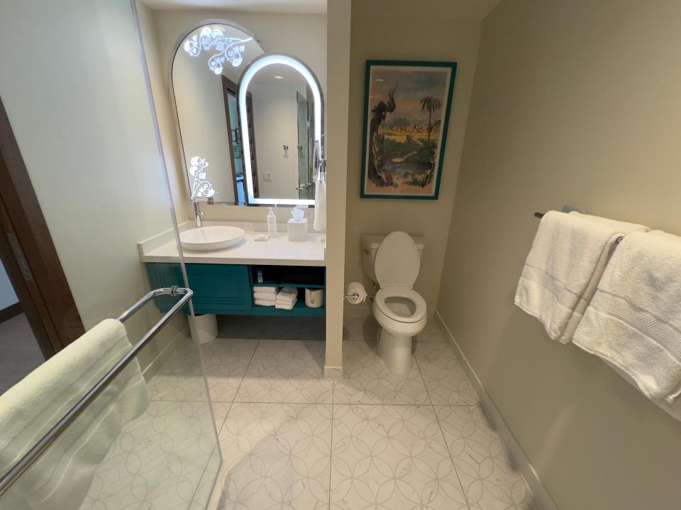 Bathroom in Disneyland Hotel duo studio with simple white toilet next to two arched mirrors above a blue vanity and white sink