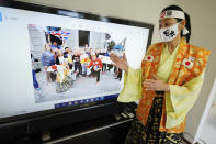 Olympic fan Kyoko Ishikawa shows an image on a TV screen showing her at London Olympics with local people Saturday, April 10, 2021, in Tokyo.Ishikawa, president of an IT company, has attended every Summer Olympics since Barcelona in 1992, becoming famous as an unofficial "International Olympic Cheerleader." She relishes joining in with fans from everywhere to cheer for their athletes. (AP Photo/Eugene Hoshiko)