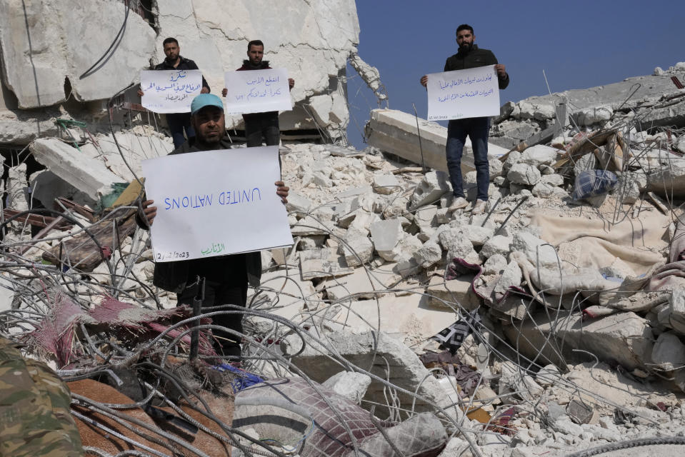 FILE - Men stand amidst the rubble of destroyed houses with placards criticizing the United Nations, in Atareb, Syria, Sunday, Feb. 12, 2023. The massive earthquake that hit last week is the latest in a litany of hardships for Syrian women, many of whom have been left dependent on aid and alone responsible for their families' well-being. (AP Photo/Hussein Malla, File)