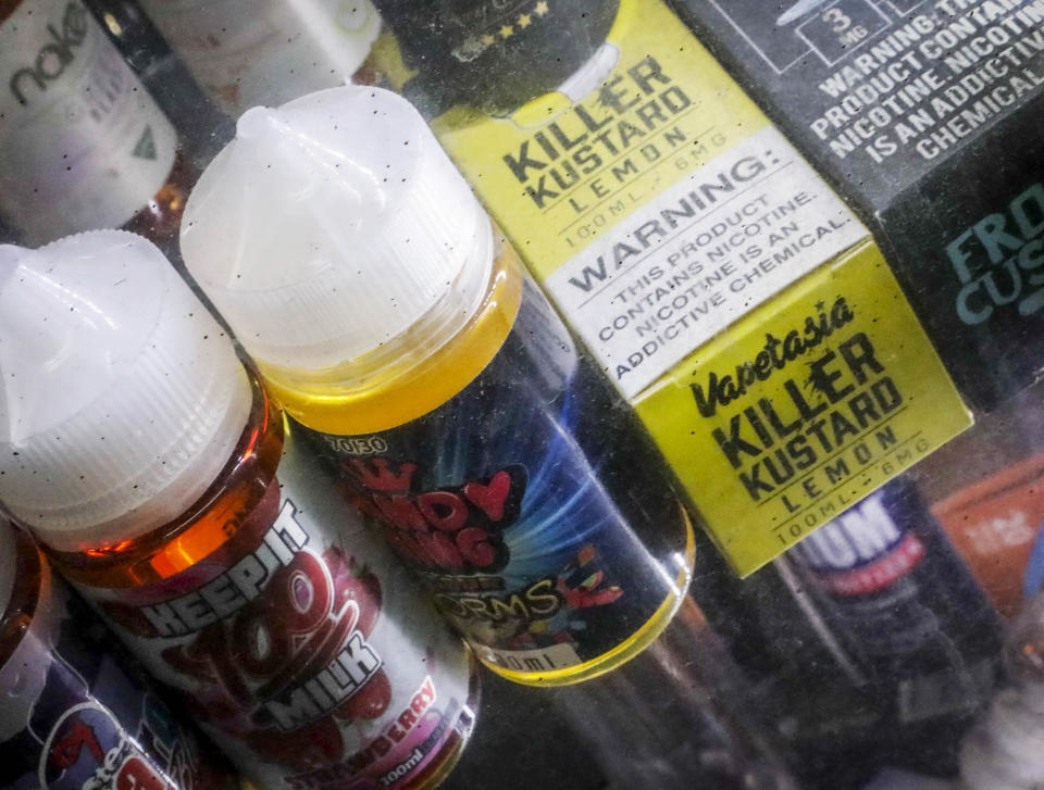 FILE- This Sept. 16, 2019 file photo shows flavored vaping solutions in a window display at a vape and smoke shop in New York. On Thursday, Jan. 2, 2020, the Trump administration announced that it will prohibit fruit, candy, mint and dessert flavors from small, cartridge-based e-cigarettes that are popular with high school students. But menthol and tobacco-flavored e-cigarettes will be allowed to remain on the market. The flavor ban will also entirely exempt large, tank-based vaping devices, which are primarily sold in vape shops that cater to adult smokers. (AP Photo/Bebeto Matthews, File)