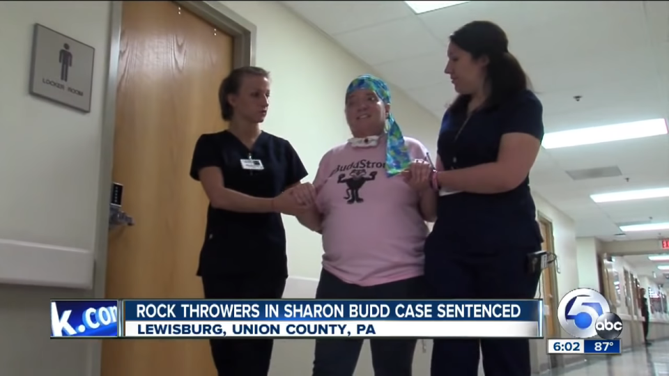 Two healthcare workers assist a woman walking in a hospital corridor. News banner about a legal sentence at the bottom