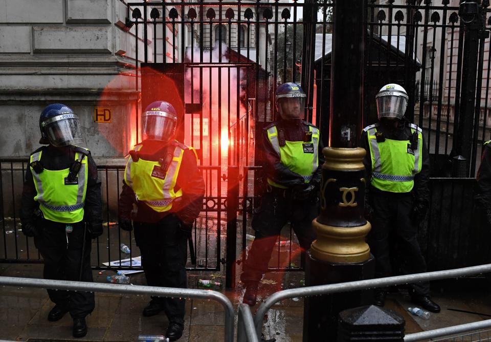 Police officers in riot gear stand on duty as a flare, thrown by protesters, burns inside Downing Street, during an anti-racism demonstration in central London on June 6, 2020, to show solidarity with the Black Lives Matter movement in the wake of the killing of George Floyd, an unarmed black man who died after a police officer knelt on his neck in Minneapolis. - The United States braced Friday for massive weekend protests against racism and police brutality, as outrage soared over the latest law enforcement abuses against demonstrators that were caught on camera. With protests over last week's police killing of George Floyd, an unarmed black man, surging into a second weekend, President Donald Trump sparked fresh controversy by saying it was a "great day" for Floyd. (Photo by DANIEL LEAL-OLIVAS / AFP) (Photo by DANIEL LEAL-OLIVAS/AFP via Getty Images)