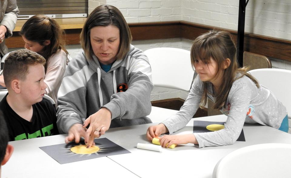 Bethany Clark and her children Arden, 11, and Olivia, 10, of West Lafayette work on a craft at the Coshocton County District Library during a presentation for youth on the upcoming solar eclipse.