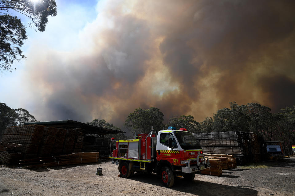 Firefighters, from Fire and Rescue NSW and NSW Rural Fire Service, help defend a property near Colo Heights. A fire truck is seen in the foreground as smoke billows above it.