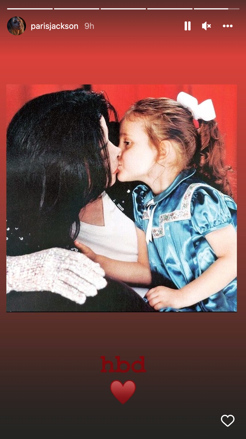 Young Paris Jackson gives her father a kiss. She wears a blue satin dress with a bow in his hair.