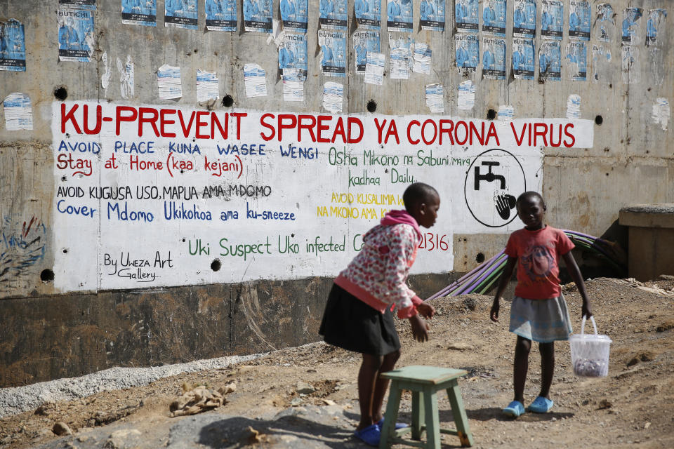 Two young girls sell groundnuts in front of an informational mural advising on precautions to avoid catching the new coronavirus, in the Kibera slum, or informal settlement, of Nairobi, Kenya Thursday, April 2, 2020. Writing on wall in Swahili reads "To prevent the spread of coronavirus avoid congested places, stay at home, don't touch your nose, cover your mouth while coughing, wash your hands, call emergency toll free line when you suspect the symptoms". (AP Photo/Brian Inganga)