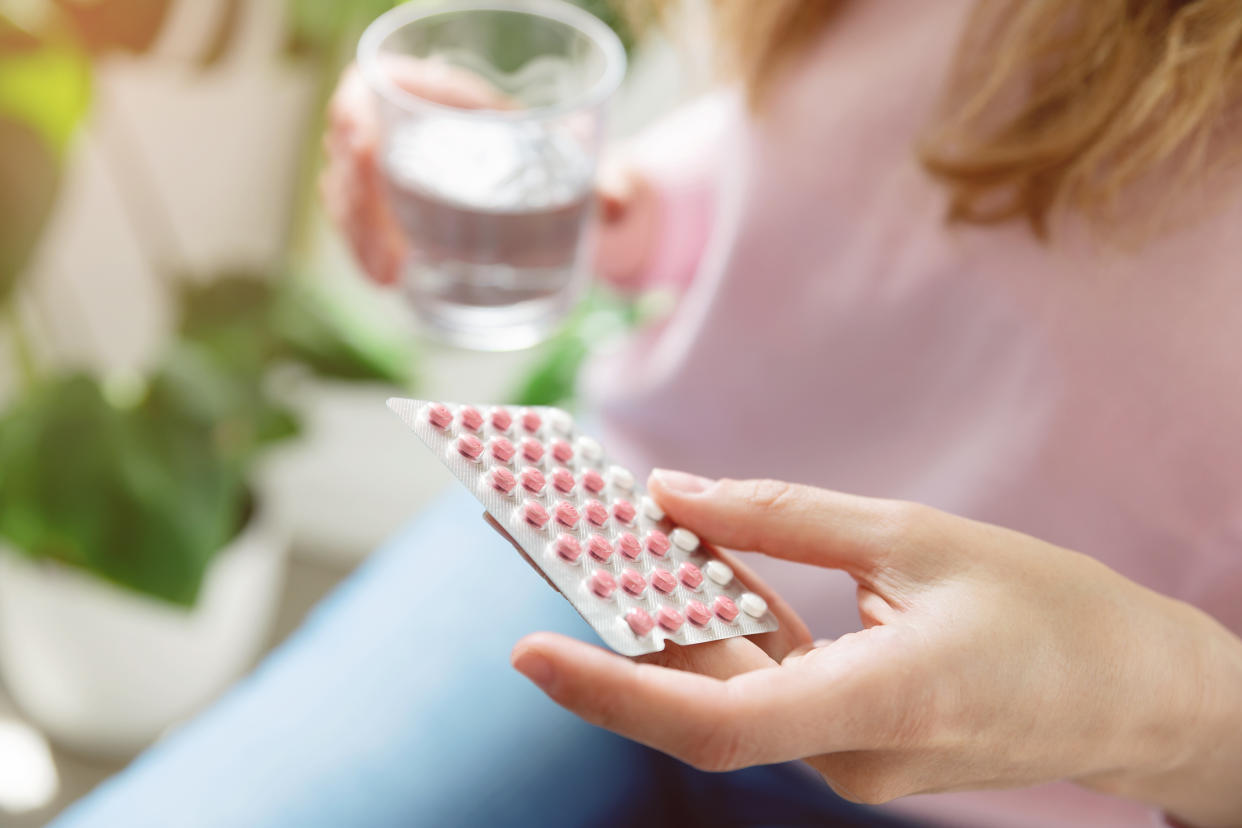 Close up of woman holding contraceptive pill and glass of water at home