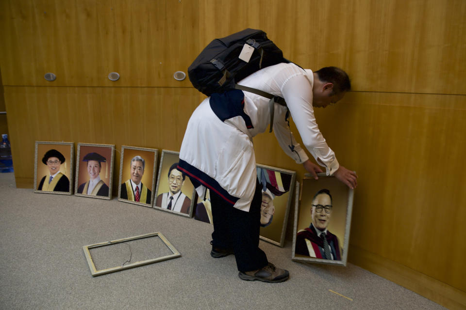 Prof. Alex Wai, a vice president with the Hong Kong Polytechnic University sets upright portraits of former university council chairperson as he leads a team to look for holed up protesters on the university campus in Hong Kong, Tuesday, Nov. 26, 2019. Hong Kong's embattled leader Carrie Lam refused to offer any concessions to anti-government protesters despite a local election trouncing, saying Tuesday that she will instead accelerate dialogue and identify ways to address societal grievances. (AP Photo/Ng Han Guan)