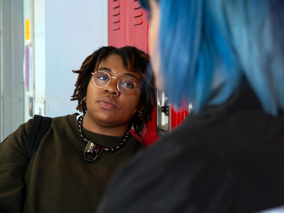 A non binary student talking to a friend in front of their locker