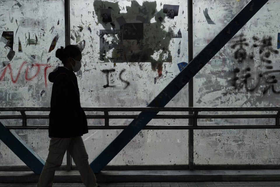 In this Monday, Feb. 10, 2020, photo, a woman wearing a protective face mask walks past peeled off posters made by pro-democracy protesters at a footbridge in Hong Kong. The city's often-tumultuous street protests had already slowed in the past two months. Now they have ground to an almost complete halt as attention focuses on how to avoid a recurrence of the SARS pandemic, which killed about 300 people in Hong Kong in 2002-03. (AP Photo/Vincent Yu)