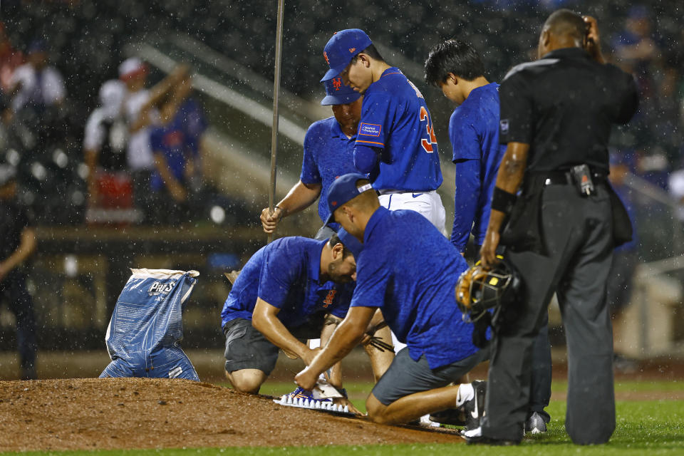 New York Mets starting pitcher Kodai Senga (34) watches in the rain as the grounds crew attempts to dry the mound before the top of the seventh inning of a baseball game against the Chicago Cubs, Monday, Aug.7, 2023, in New York. The ground crew worked on the mound but the decision was made to delay the game. (AP Photo/Rich Schultz)