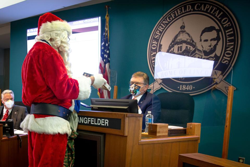 Santa Claus, portrayed by Rich Berning, hands a gift to Springfield Mayor Jim Langfelder while giving gifts to the Springfield City Council in the council chamber Tuesday. [Justin L. Fowler/The State Journal-Register]