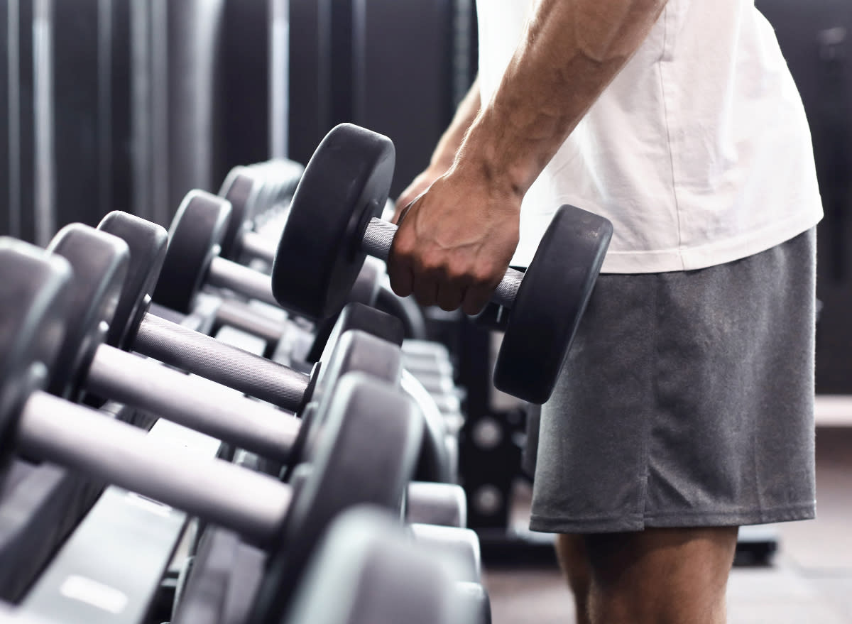 man grabbing dumbbells from rack at gym, close-up