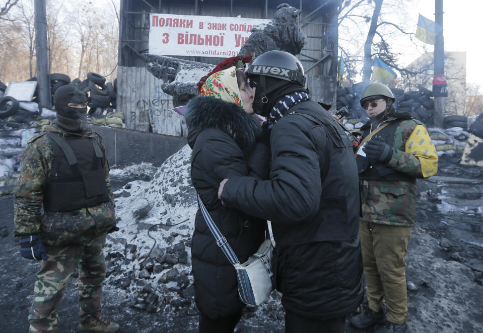 An opposition supporter, center right, kisses his girlfriend, asking her to marry him while two other activists dressed in a protective clothes act as witnesses to a 'ceremony' at barricades in central Kiev, the epicenter of the country's current unrest, Ukraine, Sunday, Feb. 2, 2014. The supporter took his bride specially to barricades to share a tender moment there. Kitted out in masks, helmets and protective gear on the arms and legs, radical activists are the wild card of the Ukraine protests now starting their third month, declaring they're ready to resume violence if the stalemate persists.(AP Photo/Efrem Lukatsky)