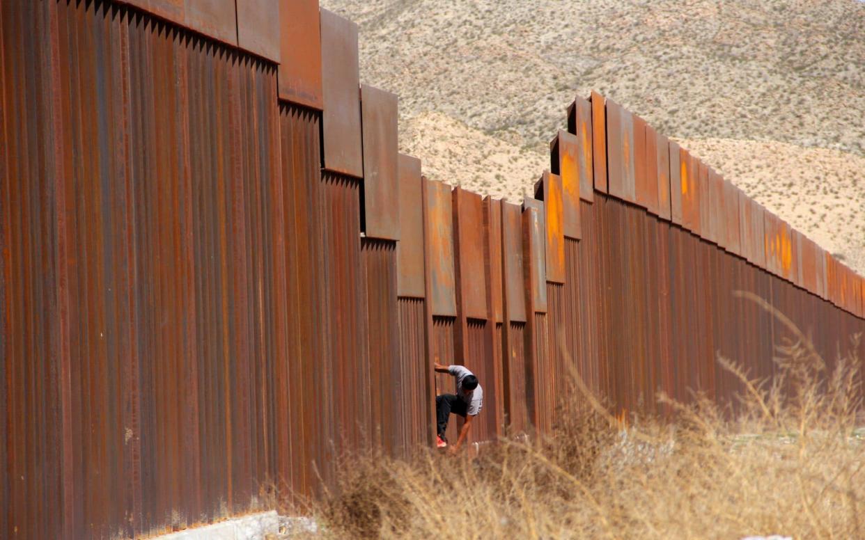 Young Mexicans help a compatriot to climb the metal wall that divides the border between Mexico and the United States  - AFP