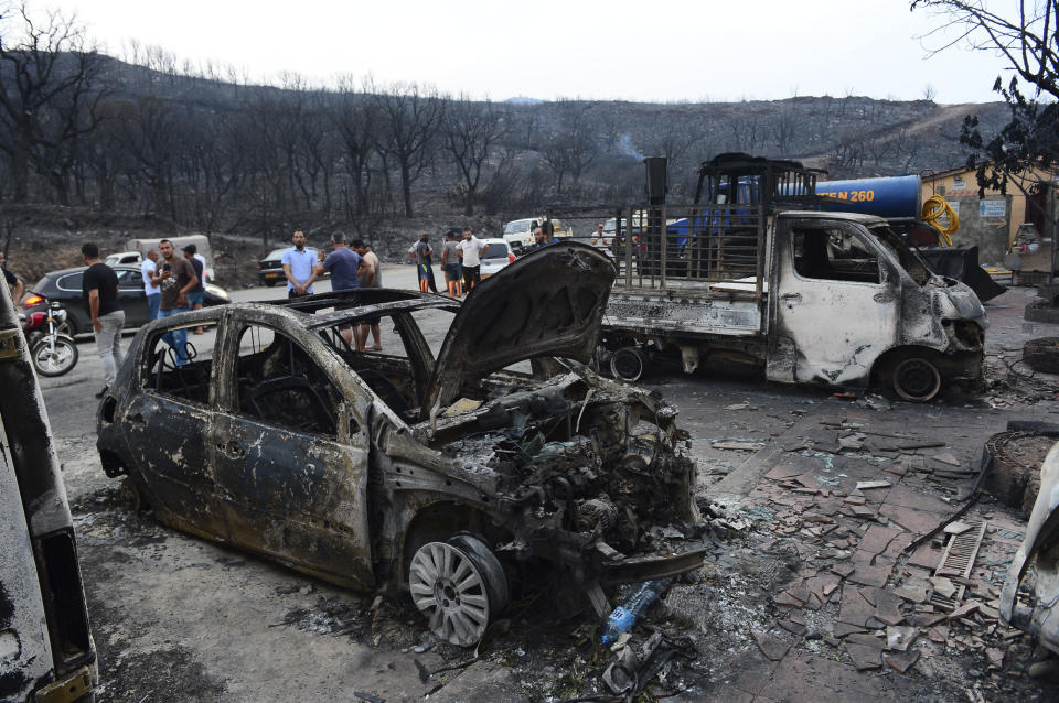 People inspect burnt vehicles after raging wildfires in Bouira, 100 km from Algiers, Algeria, Monday, July 24, 2023. Wildfires raging across Algeria have killed at least 25 people, including soldiers trying to get the flames under control in the face of high winds and scorching summer temperatures, government ministries said Monday. (AP Photo)