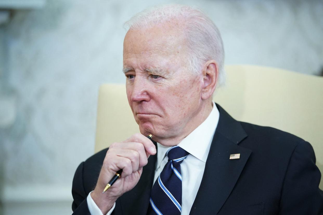 President Biden holds a pen in thought as he sits in the Oval Office.