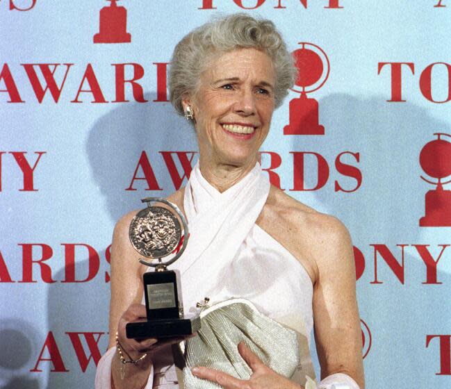 Frances Sternhagen smiles and holds her Tony award while wearing a white dress and clutches a silver hand bag