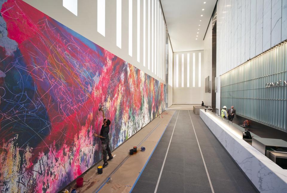 Inside the lobby of One World Trade Center in New York City, José Parlá is photographed working on a 90-foot long mural titled ONE: Union of the Senses (Parlá worked on the piece for eight months in his studio and two weeks on-site).
