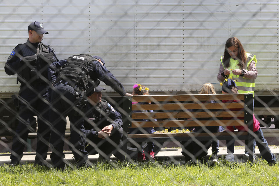 A police officer decorates a girl with dandelions as she plays with a group of children at a detention center where authorities have brought back from Syria 110 Kosovar citizens, mostly women and children in the village of Vranidol on Sunday, April 20, 2019. Four suspected fighters have been arrested, but other returnees will be cared for, before being sent to homes over the coming days, according to Justice Minister Abelard Tahiri.(AP Photo/Visar Kryeziu)