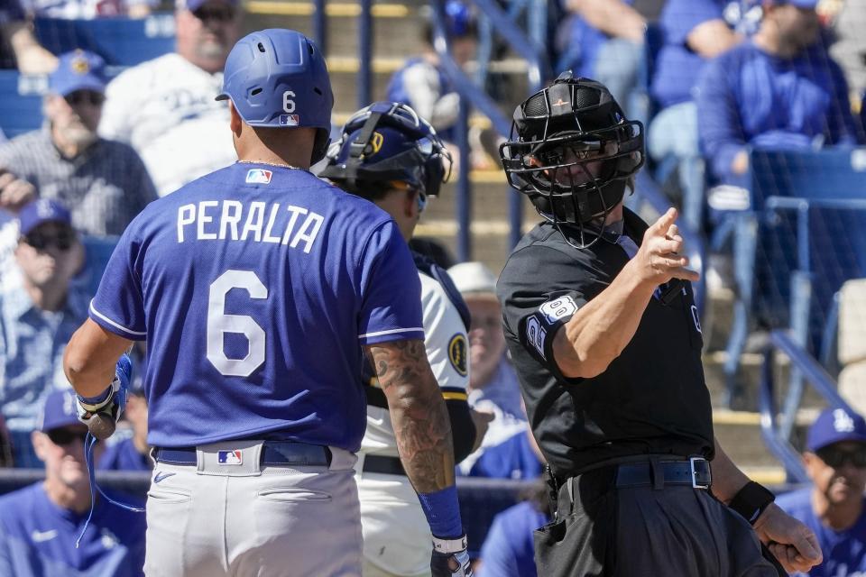 Home plate umpire Jim Wolf tells Los Angeles Dodgers' David Peralta to take a base after a pitching clock violation during the second inning of a spring training baseball game against the Milwaukee Brewers Saturday, Feb. 25, 2023, in Phoenix. (AP Photo/Morry Gash)