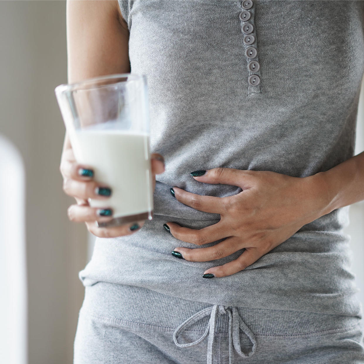 woman clenching her stomach holding a glass of milk