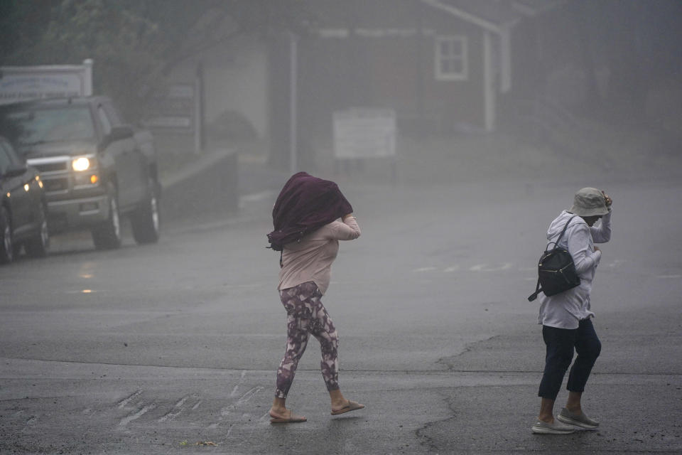 Two people cross the road as wind and rain pummel the area Friday, Sept. 9, 2022, in Julian, Calif. A tropical storm nearing Southern California has brought fierce mountain winds, high humidity, rain and the threat of flooding to a region already dealing with wildfires and an extraordinary heat wave. (AP Photo/Gregory Bull)