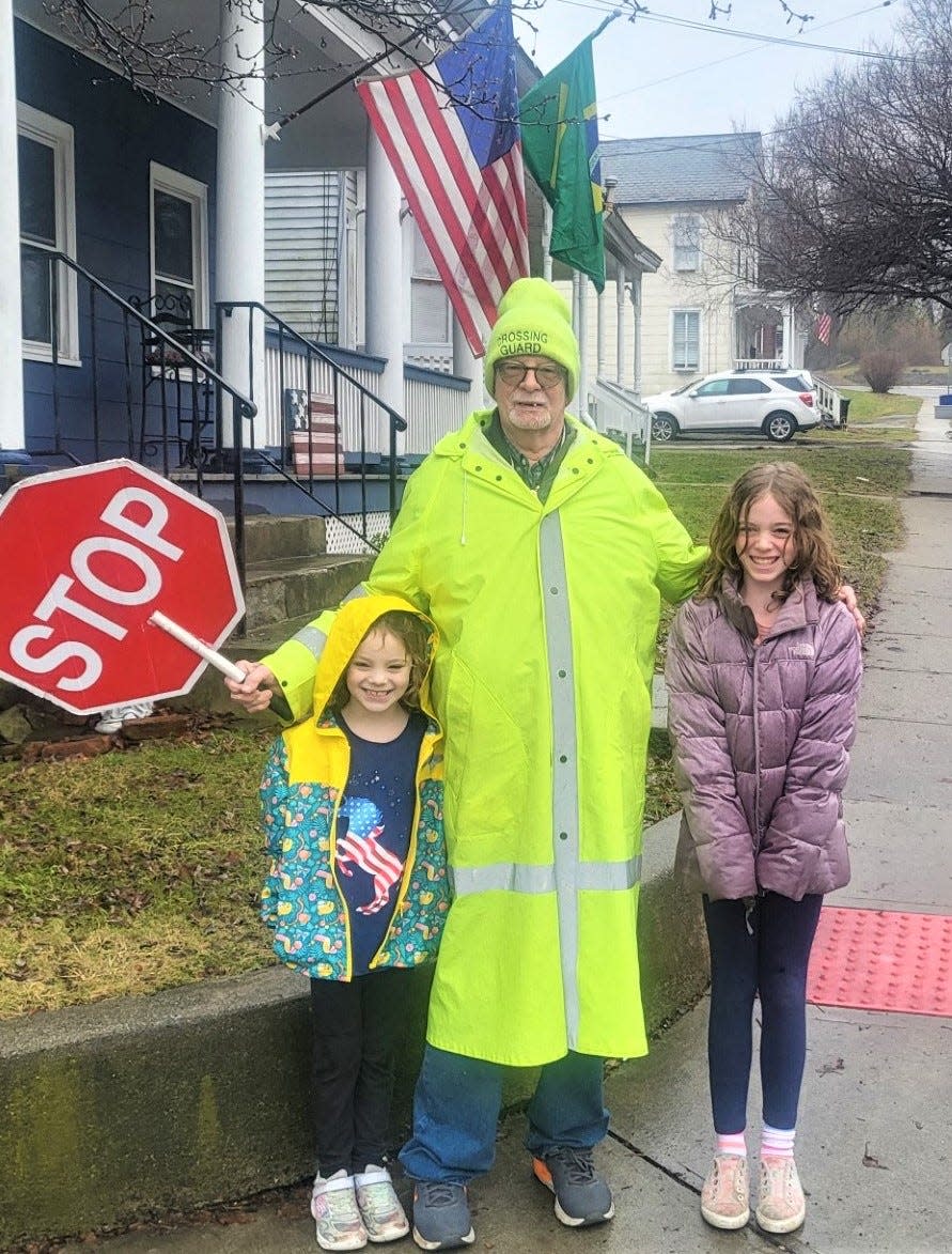 Lily Atkinson, 9, right, and her younger sister, Charlotte, 6, pose with Newton school crossing guard and Army veteran Harry Kaplan at his crossing post at Division and High streets. The Atkinsons have purchased two banners honoring Kaplan and next-door neighbor Wallace Struble, as part of the town's Hometown Heroes program.
