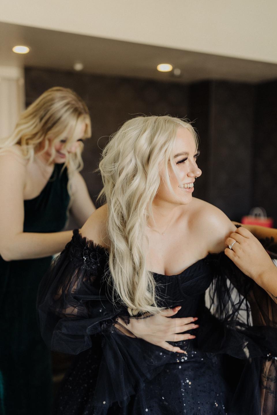 A bride smiles as someone helps her into her black wedding dress.