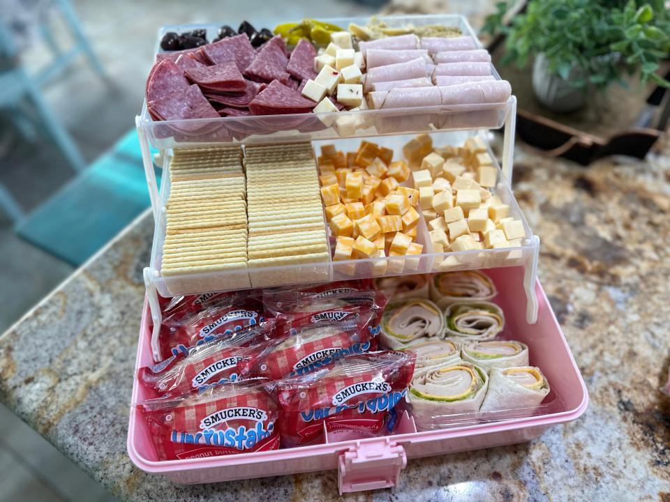 A plastic box featuring an array of Crustable sandwiches, wraps with meat, cheese, salami, and crackers.