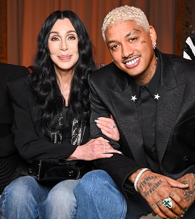 Cher in a black top and jeans holds on to boyfriend Alexander Edwards at the Balmain show