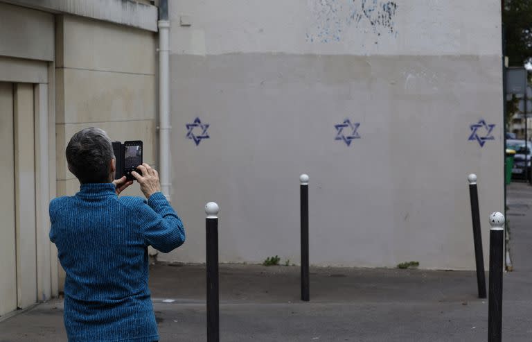 A woman uses a smartphone to take photos of a building wall covered with Stars of David painted during the night, in the Alesia district of Paris, on October 31, 2023. (Photo by Geoffroy VAN DER HASSELT / AFP)